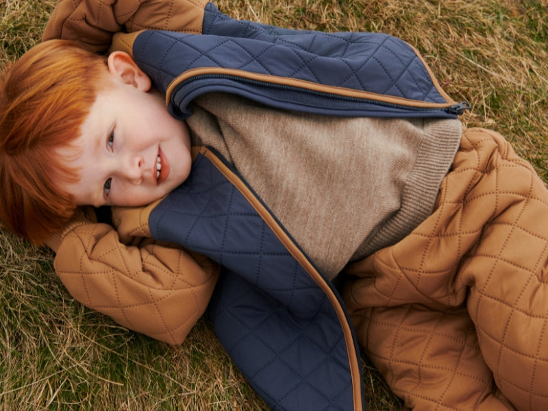 Child wearing a quilted jacket lying on grass